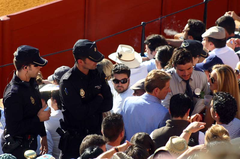 Dos policías observan cómo un vigilante intenta informar a un espectador sobre la ubicación de su localidad.