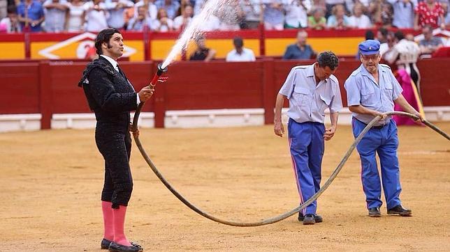 Morante, con la ayuda de dos operarios de la plaza, riega el albero de Alicante durante la 'merienda', en el ecuador del festejo. (FOTO: mundotoro.com)