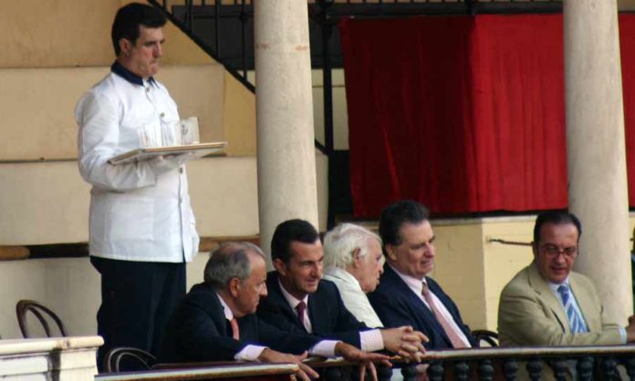 Un camarero con una bandeja con vasos de cristal junto a un grupo de maestrantes. (FOTO: Sevilla Taurina)