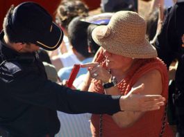 Una señora mayor señala a su asiento para poder acceder, y el policía le corta el paso indicándole que baje a los pasillos interiores.